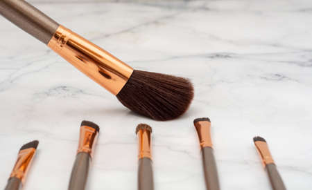 Large makeup brush, along with other smaller balls, with a spatula on a marble base