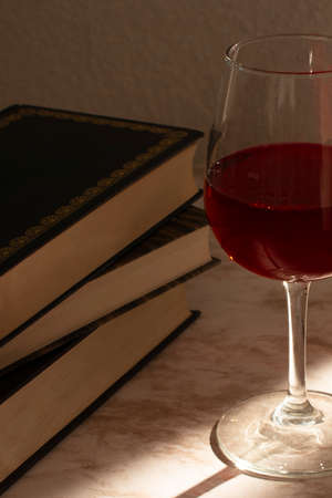 Glass of wine accompanied by some books with the light of the sale entering from the sideの写真素材
