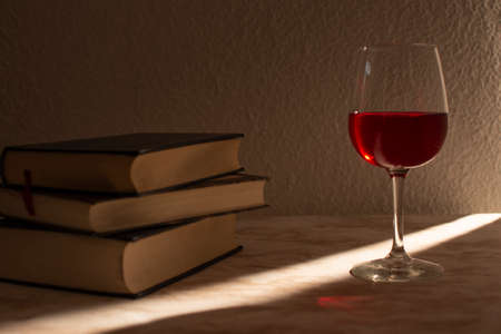 Glass of wine accompanied by some books with the light of the sale entering from the sideの写真素材