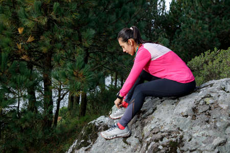 Athlete tying tennis laces on the shore of a lake after running in nature