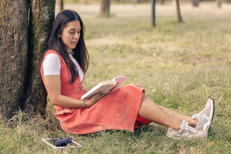 Latin woman reading an ornate book from a tree., In the park. Outdoor recreation conceptの写真素材