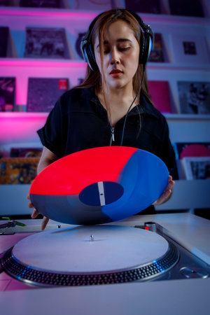 Beautiful Latin girl with headphones changing a vinyl record on the turntable. Dj girl concept in vinyl record storeの写真素材