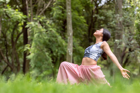 Mexican woman doing Yoga with different postures, in the outdoor park with grass and trees in the...