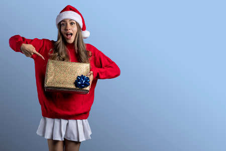 Young Latin woman with Christmas clothes with a gift in her hands and space for textの写真素材