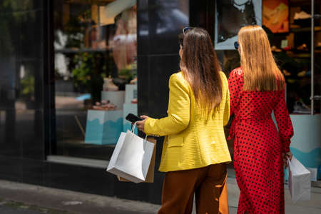 Rear view portrait of two shopping women walking down the street in shopping areaの写真素材