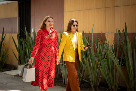 Two happy girlfriends shopping in the city walking down the street carrying their shopping bagsの写真素材