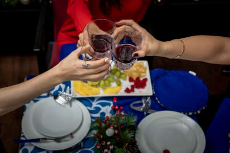 top view of hands with glasses toasting at a christmas dinner, with christmas decoration in the...