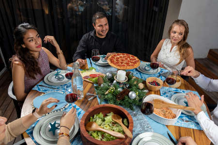 Friends chatting joyfully sitting at a table with blue decoration, at christmas dinnerの写真素材