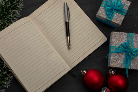 Open notebook with a pen on a black wooden background and Christmas decorationの写真素材