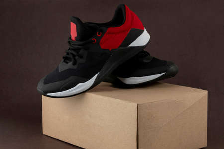 Pair of black and red sports tennis shoes, placed on their cardboard box