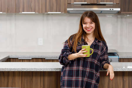 Cheerful woman at home with comfortable clothes having a cup of coffee in her kitchen
