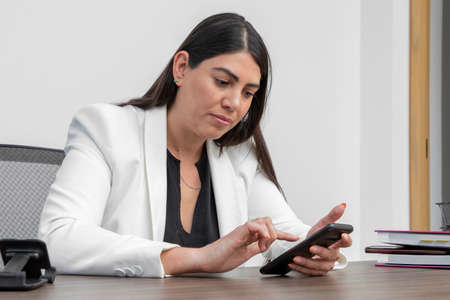 Business woman checking her cell phone while working in her office. Woman in formal wear checking her mobile phone.の写真素材
