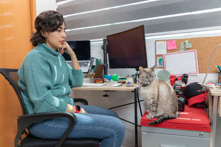 Young Latina woman watching her cat while she takes a break from work at home