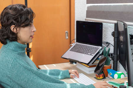Young Latina woman with a smile works on her computer from home. Home-office concept.の写真素材