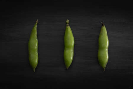 three broad beans in shell lined up on a black wooden backgroundの写真素材