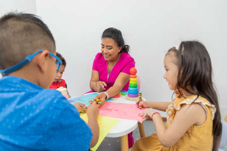 Female pediatrician sitting at a table with several children playing in her medical officeの写真素材