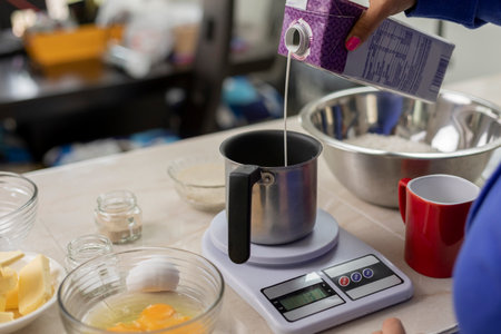 womans hand pouring milk into a container to weigh on a scale and make breadの写真素材