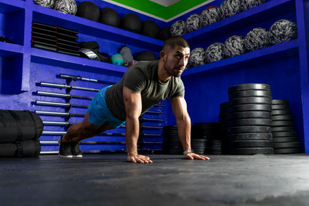 latino athlete with sportswear in a gym doing high plankの写真素材
