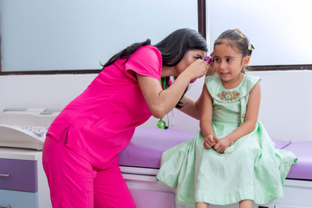 Pediatrician doctor checking the ear of a little girl in her medical officeの写真素材