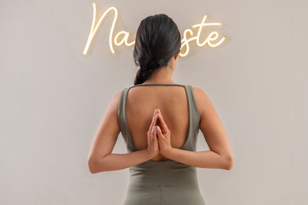 Young mexican woman with palms together behind her back doing namaste gesture