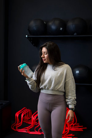 Sports trainer shaking her shaker with protein to take before training at the gym.