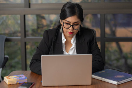 Serious woman with glasses working on her laptop inside her work officeの写真素材