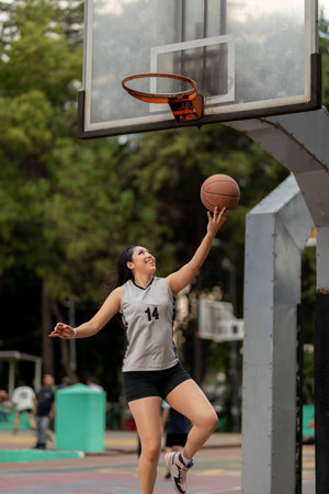 Female basketball player shooting ball into hoop on outdoor courtの写真素材