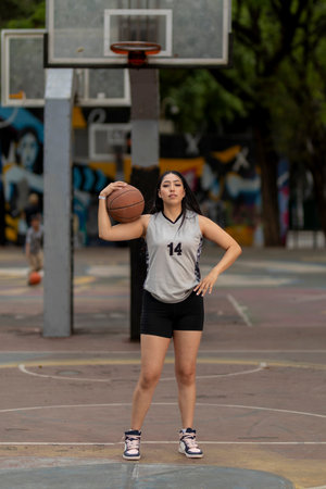 Female basketball player posing on outdoor court holding ballの写真素材