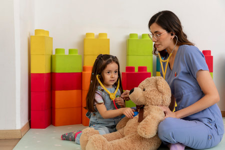 Pediatrician and girl playing doctor with teddy bear in a colorful playroomの写真素材