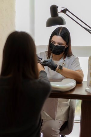 Beautician polishing nails of client wearing mask in beauty salonの写真素材