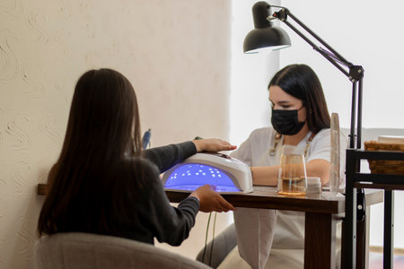 Beautician applying nail polish and drying nails of client using uv lampの写真素材