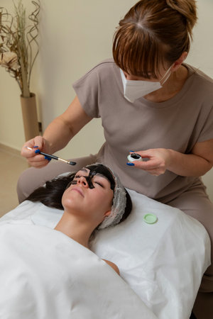 Beautician applying black mask treatment to clients face in spaの写真素材
