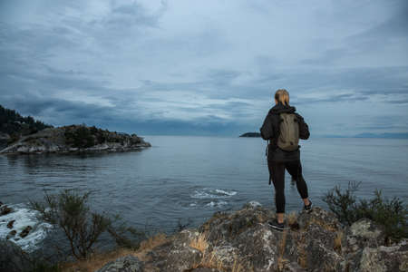 Woman exploring the coast during a cloudy sunset. Taken at Whytecliff Park, West Vancouver, British Columbia, Canada.の写真素材
