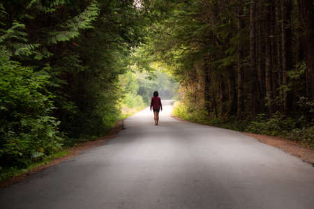 Woman walking on the scenic forest road during a vibrant summer day. Taken in Florencia Bay, near...