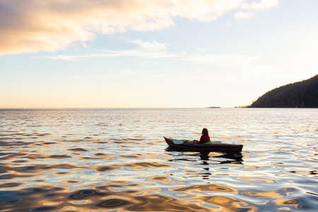 Girl kayaking in the Pacific Ocean during a cloudy summer sunset. Taken in San Josef Bay, Cape Scott, Northern Vancouver Island, BC, Canada.の写真素材