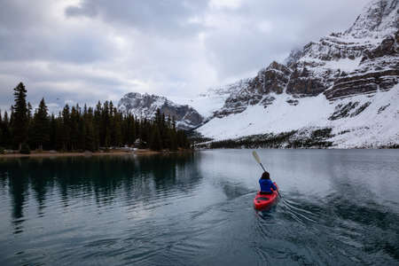 Adventurous girl kayaking in a glacier lake surrounded by the Canadian Rockies during a cloudy morning. Taken at Bow Lake, Banff, Alberta, Canada.の写真素材