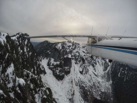 Aerial view of a small airplane flying over the Canadian Mountain Landscape during a gloomy cloudy...