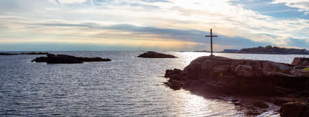 Panoramic seascape view of a cross on a rocky shore during a vibrant sunset. Taken on the Atlantic...