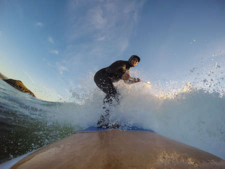 Adventurous Man Surfer on a paddle board is surfing in the ocean during a sunny sunset in Fall...