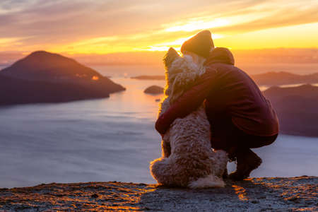 Adventurous Girl Hiking on top of a Mountain with a dog during a colorful sunset. Taken on Tunnel Bluffs Hike, near Vancouver and Squamish, British Columbia, Canada.の写真素材