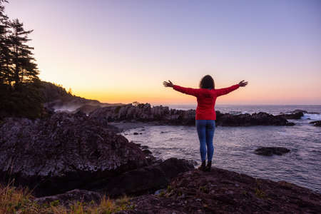 Adventurous Girl Enjoyin the Beautiful View of the Rocky Ocean Coast during a colorful and vibrant morning sunrise. Taken in Ucluelet, near Tofino, Vancouver Island, BC, Canada.の写真素材