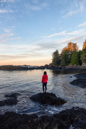 Wild Pacifc Trail, Ucluelet, Vancouver Island, BC, Canada. Girl Enjoyin the Beautiful View of the Rocky Ocean Coast during a colorful and vibrant morning sunrise.の写真素材
