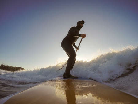 Adventurous Man Surfer on a paddle board is surfing in the ocean during a sunny morning in Fall Season. Taken in Long Beach, Tofino, Vancouver Island, BC, Canada.の写真素材