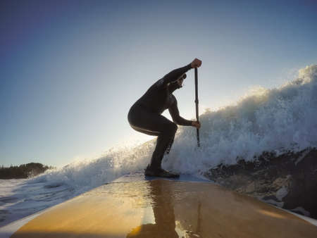 Adventurous Man Surfer on a paddle board is surfing in the ocean during a sunny morning in Fall...