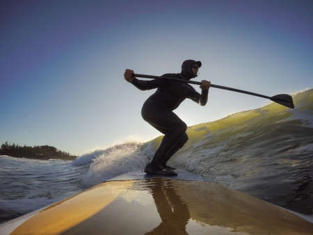 Adventurous Man Surfer on a paddle board is surfing in the ocean during a sunny morning in Fall Season. Taken in Long Beach, Tofino, Vancouver Island, BC, Canada.の写真素材