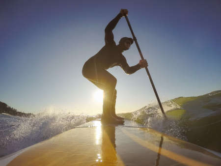 Adventurous Man Surfer on a paddle board is surfing in the ocean during a sunny morning in Fall Season. Taken in Long Beach, Tofino, Vancouver Island, BC, Canada.の写真素材