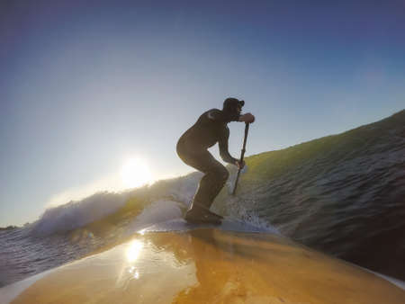 Adventurous Man Surfer on a paddle board is surfing in the ocean during a sunny morning in Fall Season. Taken in Long Beach, Tofino, Vancouver Island, BC, Canada.の写真素材