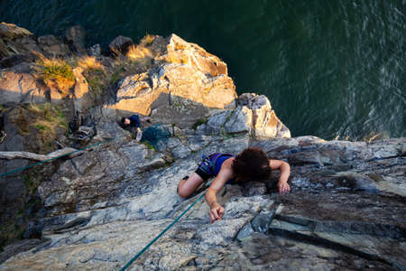 Adventurous Girl is Rock Climbing up a Steep Cliff during a summer sunset. Taken in Lighthouse Park, West Vancouver, British Columbia, Canada.の写真素材