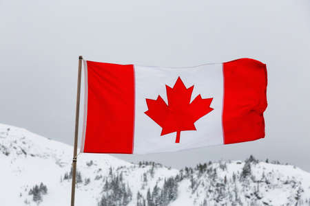 Canadian Flag with a white winter mountain landscape in the background during a foggy morning. Taken in Whistler, British Columbia, Canada.の写真素材