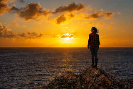 Adventurous Girl on a Rocky Ocean Coast enjoying the beautiful view of the Colorful Sunset. Image Composit. Adventure, Travel, Explore Concept.の写真素材